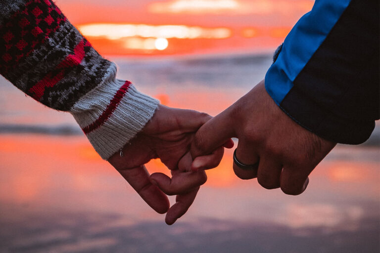 Paar hält sich an der Hand im Sonnenuntergang am Meer