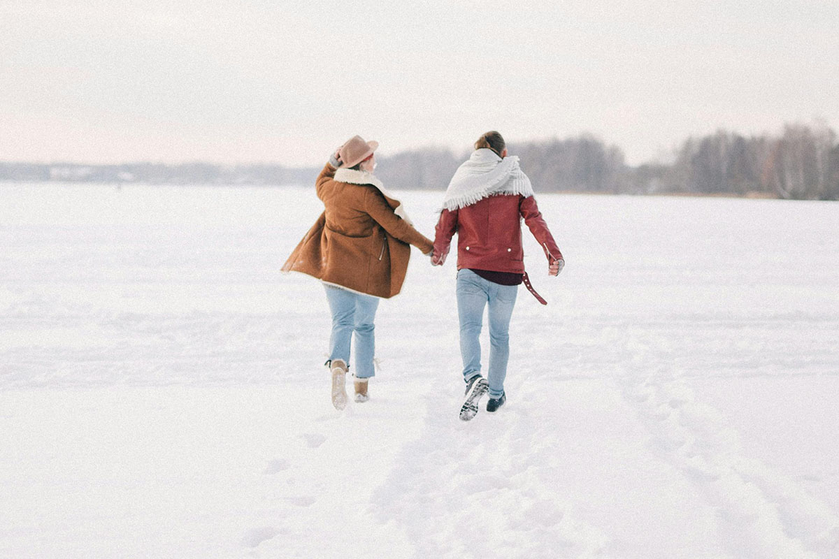 Paar läuft durch den Schnee und hält sich an der Hand.