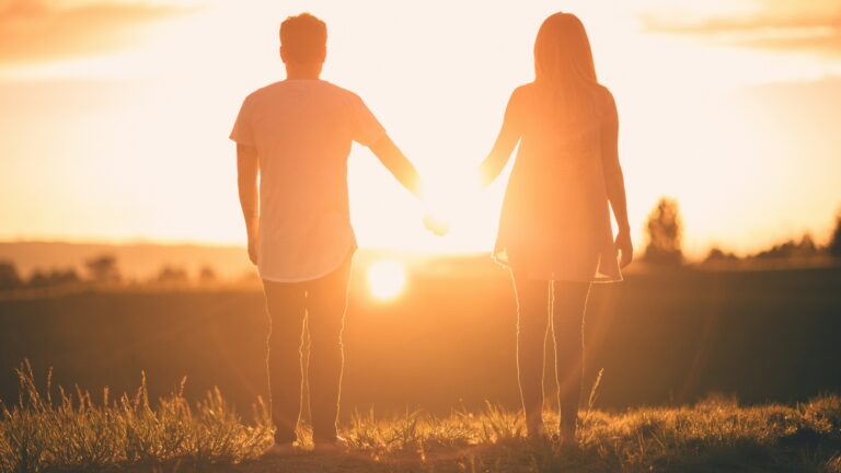 Paar geht Hand in Hand auf den Sonnenuntergang zu.